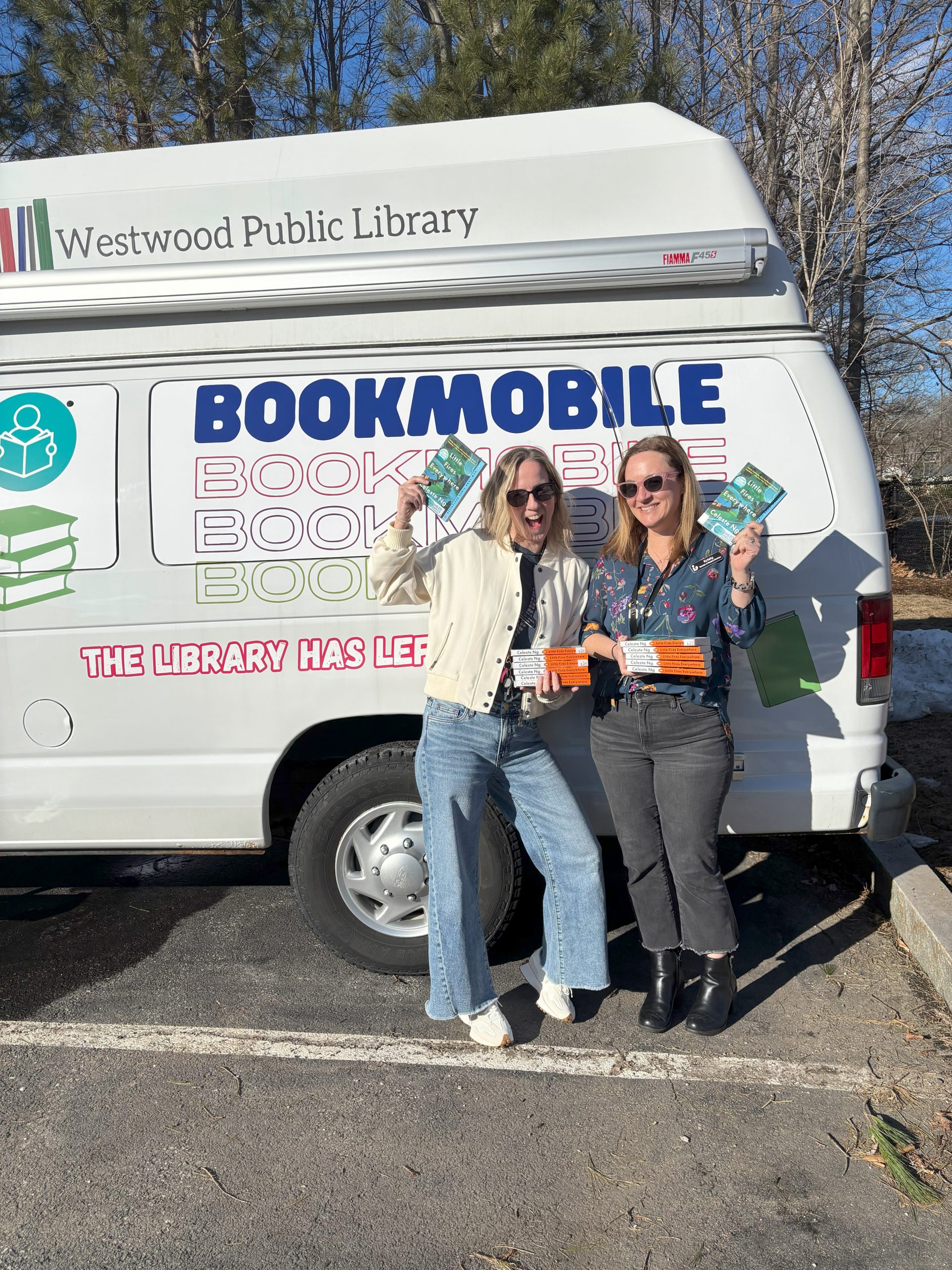 Two people holding books in front of a van